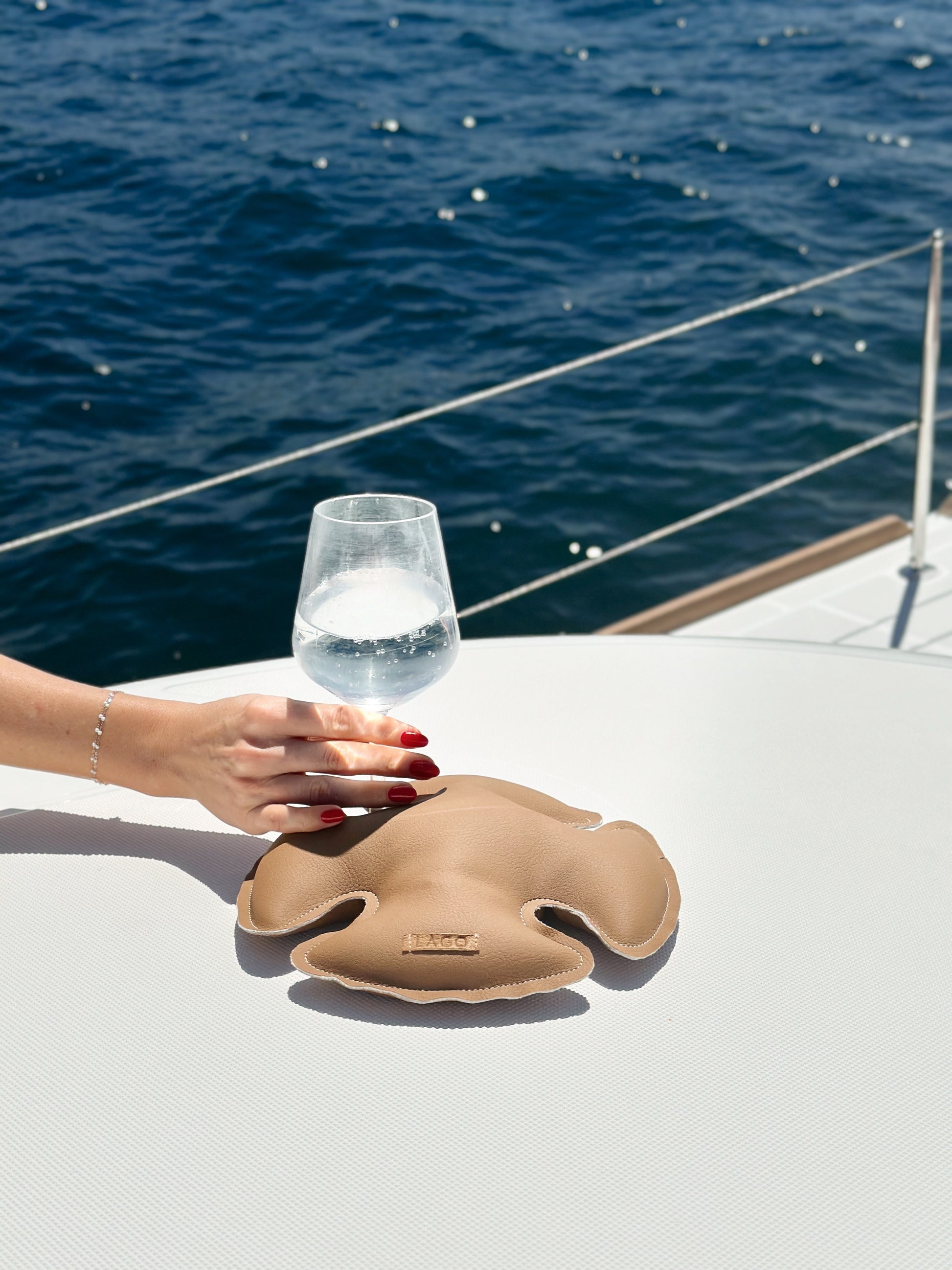 A hand steadying a wine glass on a LAGO stabilizer, set against the tranquil backdrop of open sea waters, aboard a sunlit yacht.